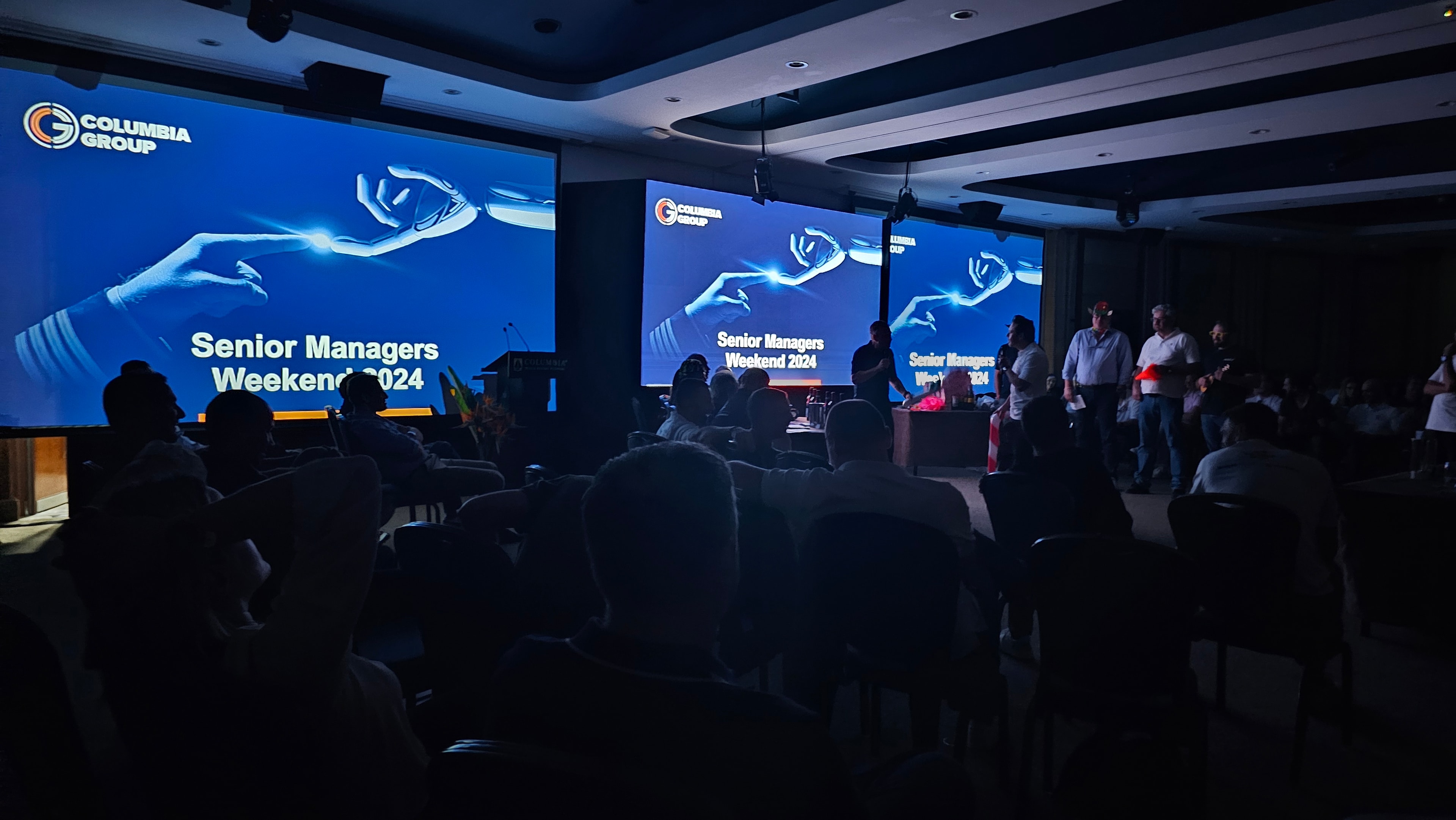 Conference presentation across three screens with seated audience