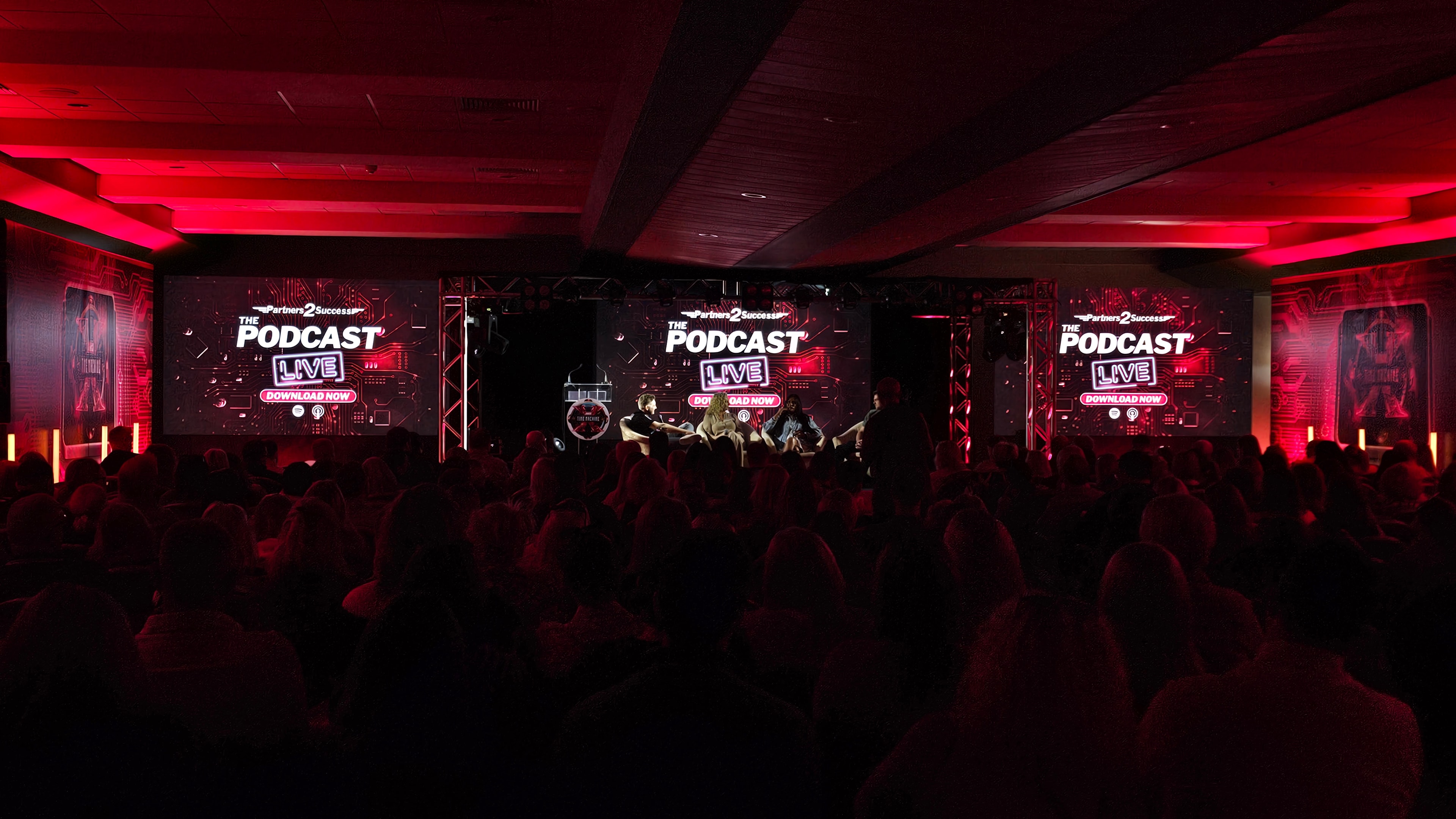 Live podcast event with red lighting, large LED displays and audience